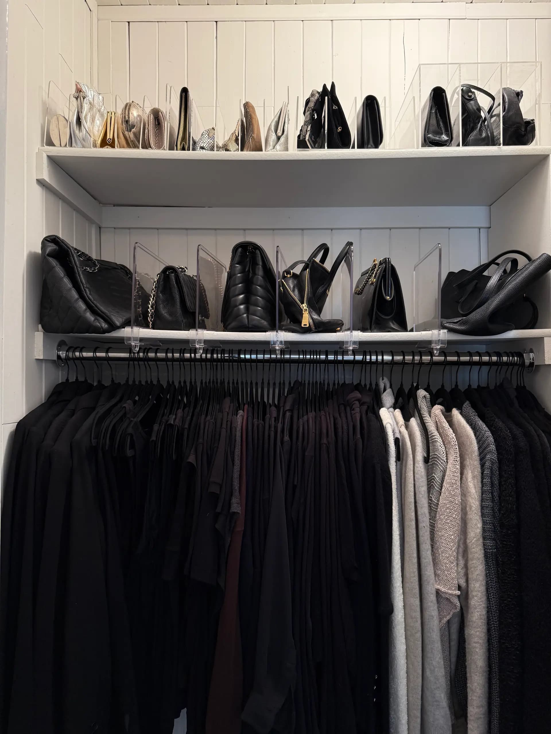 Organized walk-in closet with handbags displayed on shelves above a rack of dark clothing